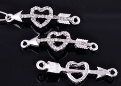 Pendentifs/entre-deux de métal, coeur avec flèche et strass ± 38x11mm (oeil ± 1,5mm). Couleur: Argenté et cristal Code: D16227 --- Coeur et fleche Strass 38x11. Argente---