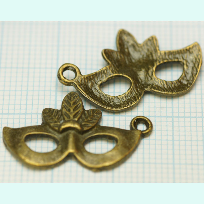 Pendentif, breloque en métal de couleur vieux bronze. +- 26 x 16mm. Œil de +- 3mm. Se vend à la pièce Code: MASQ001 --- Masque Bronze 26x16mm.---